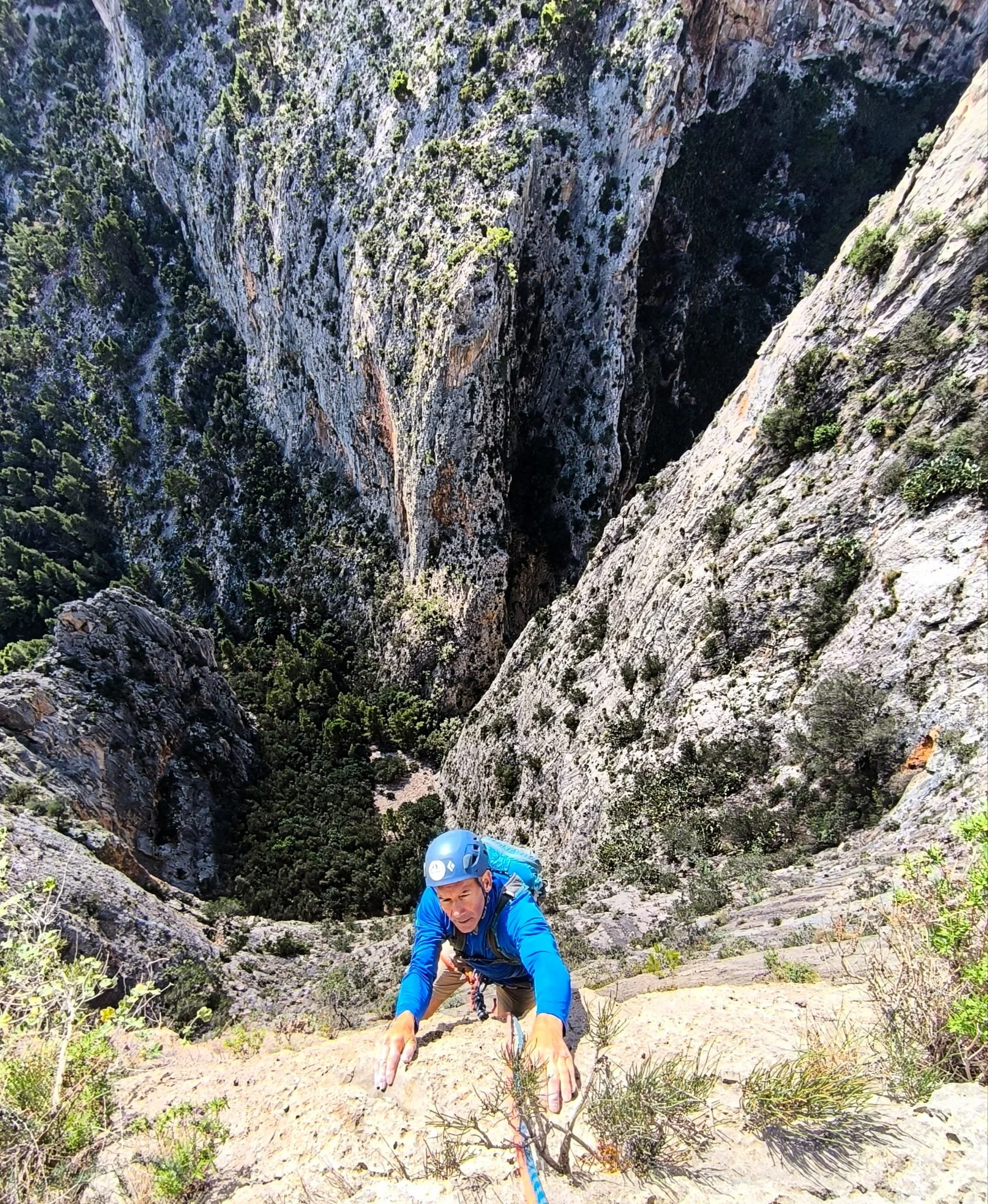A man rock climbing on a steep, rugged mountain with cliffs and greenery below.