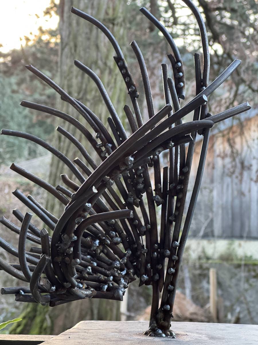 Metallskulptur mit geschwungenen Stäben im Freien vor einem unscharfen Hintergrund.