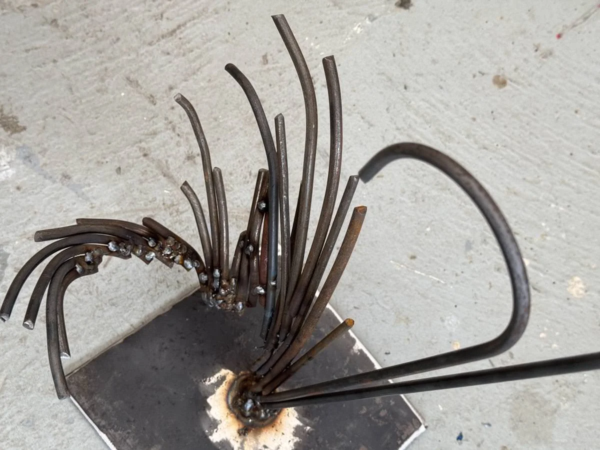 Metallskulptur mit gebogenen Stäben auf Metallplatte montiert.