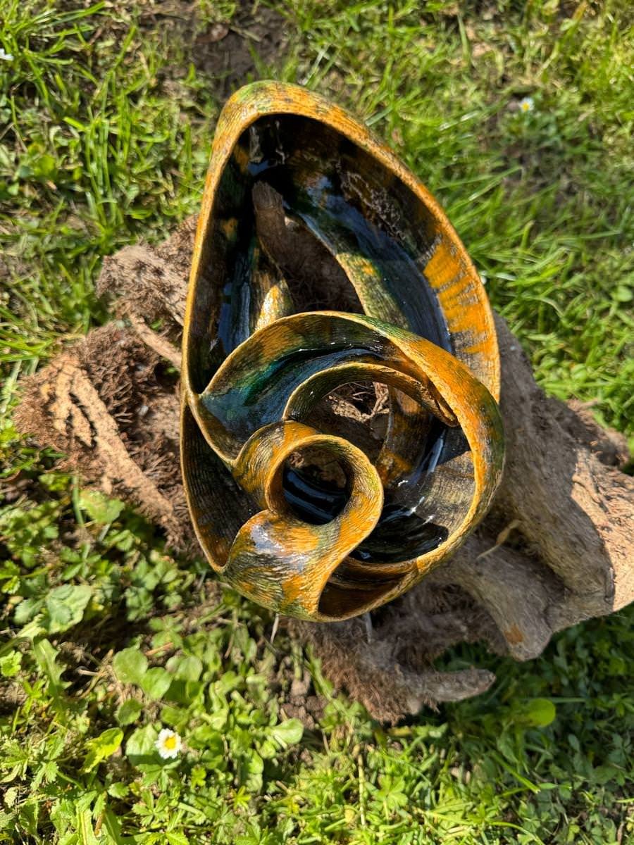 Keramikkunstwerk in organischer Form auf einem Holzstück im Gras.