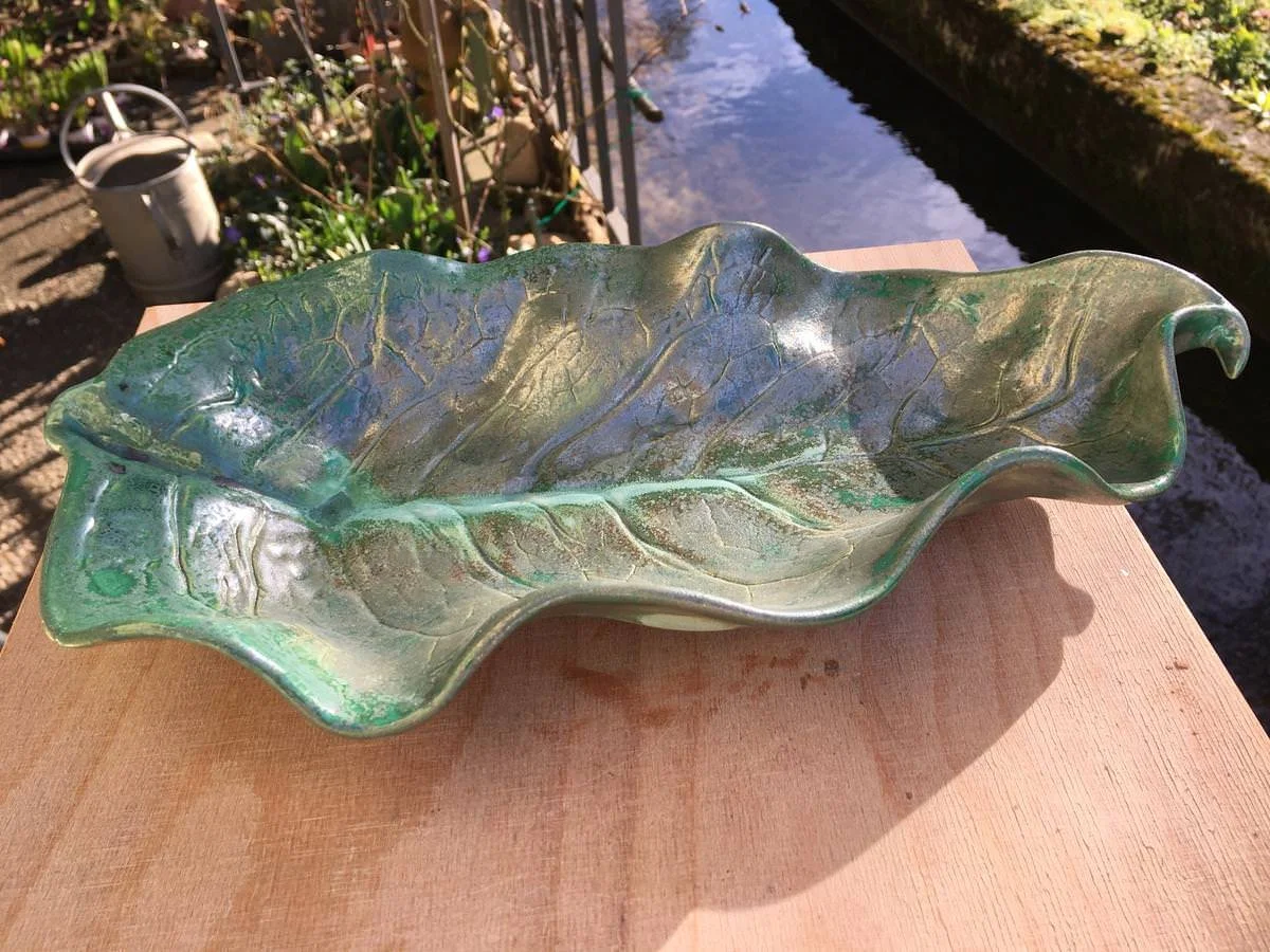 Grüne, blattförmige Keramikschale auf Holztisch im Freien platziert.