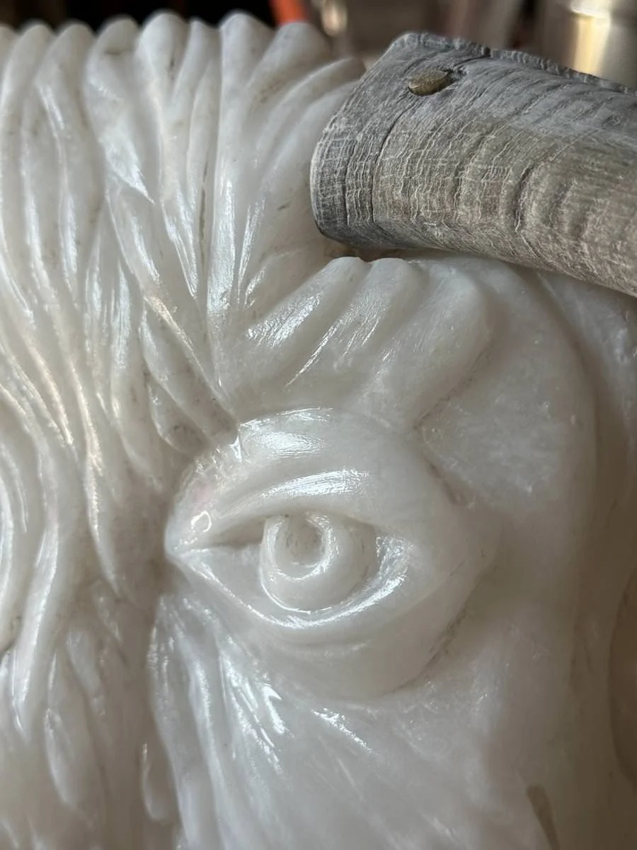 Nahaufnahme einer weißen Skulptur aus Stein mit einem Auge, daneben ein Holzgriff oder Stiel.