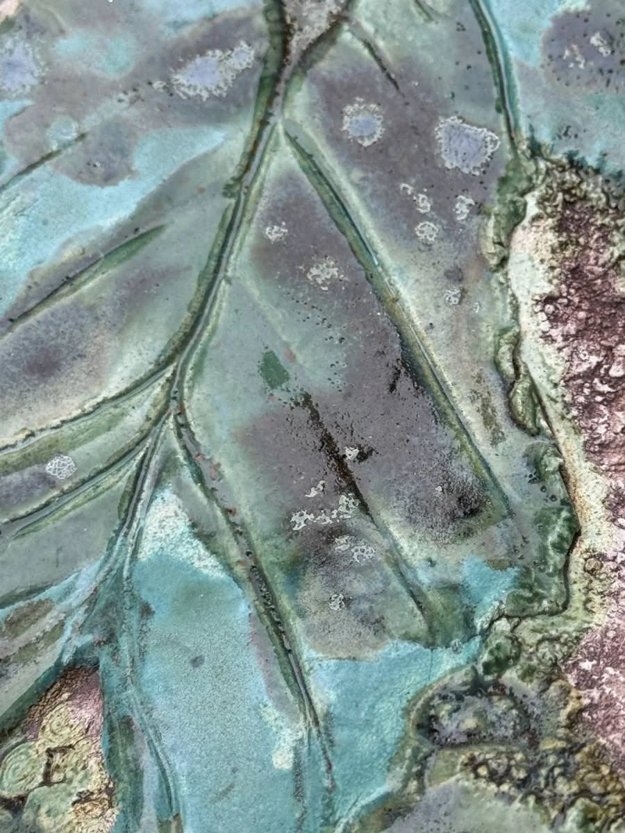 Nahaufnahme einer Keramikfliese mit Blattmuster und grüner Glasur.