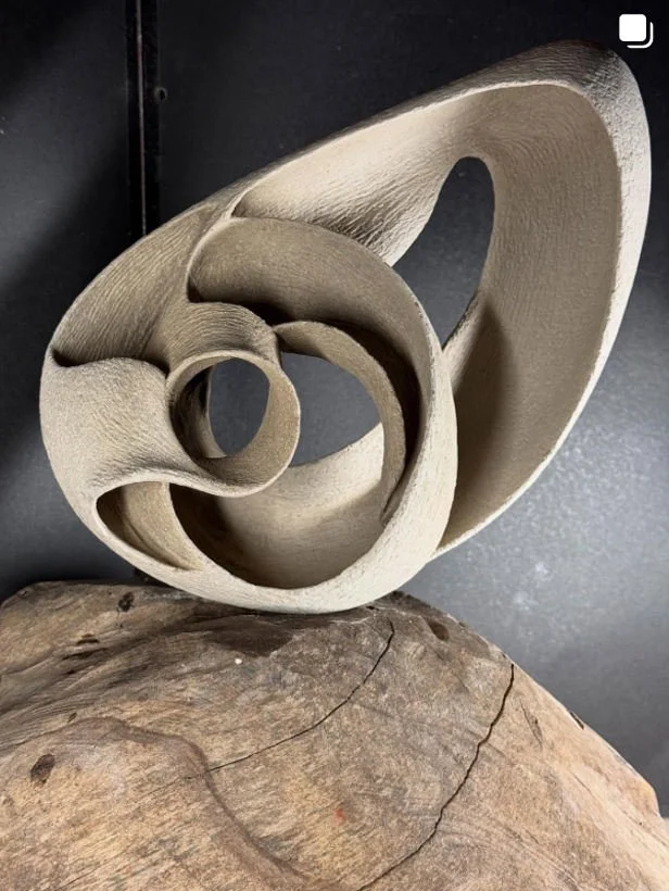 Eine abstrakte Skulptur mit geschwungenen Formen, auf einer Holzoberfläche platziert.