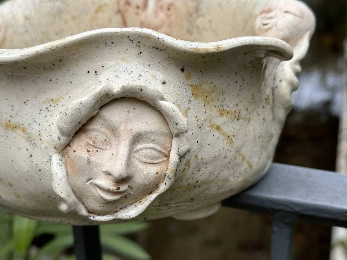 Keramikschüssel mit eingravierten Gesichtern und welligem Rand.