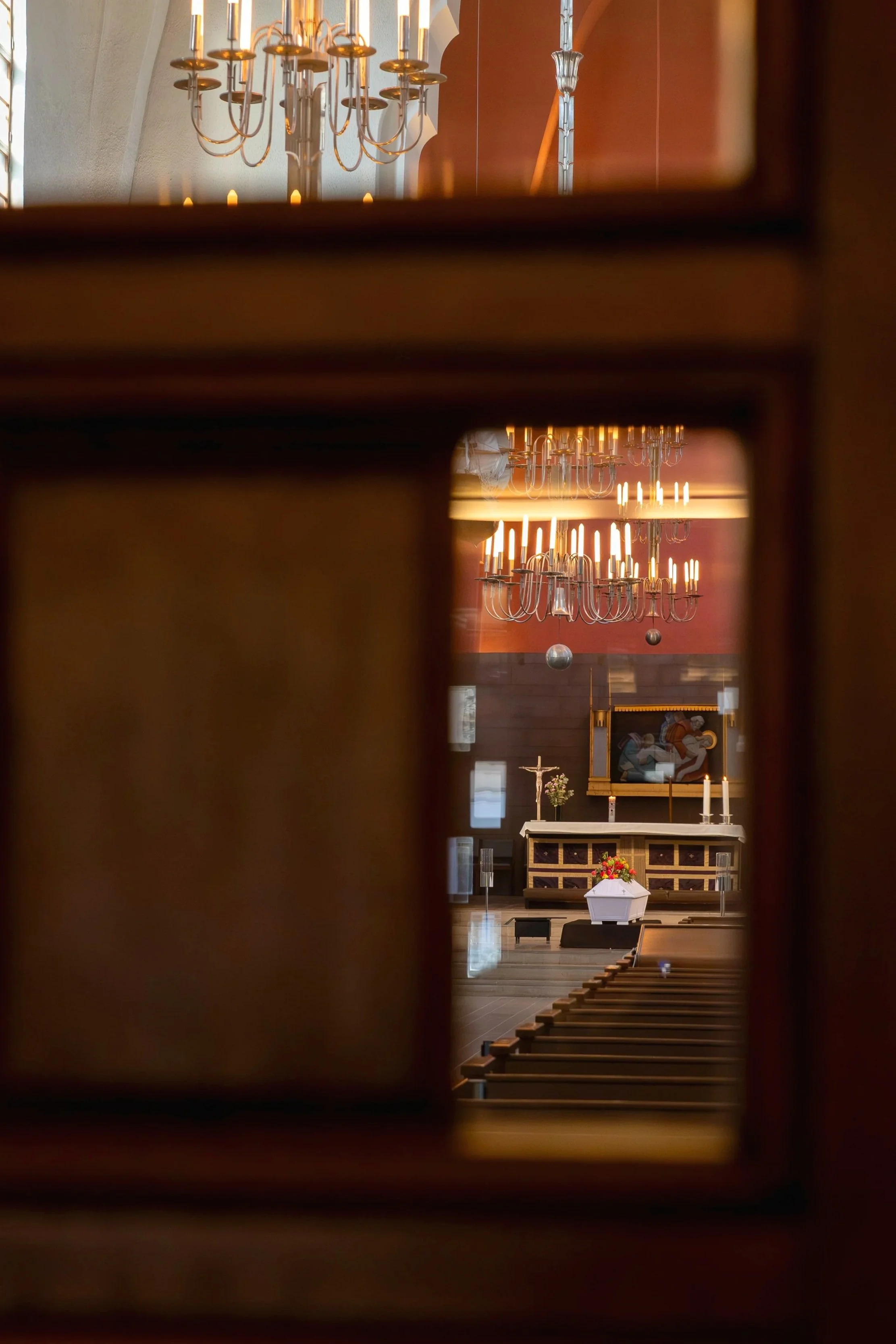 Kuvassa on hautajaiset. Kuva on otettu Mikael Agricolan kirkossa Helsingissä. Kuvassa näkyy kirkkosali, jonka etuosassa on vainajan valkoinen arkku. Kirkkosalissa ei ole vielä omaisia. Kuvan on ottanut valokuvaaja Iina Ikävalko.