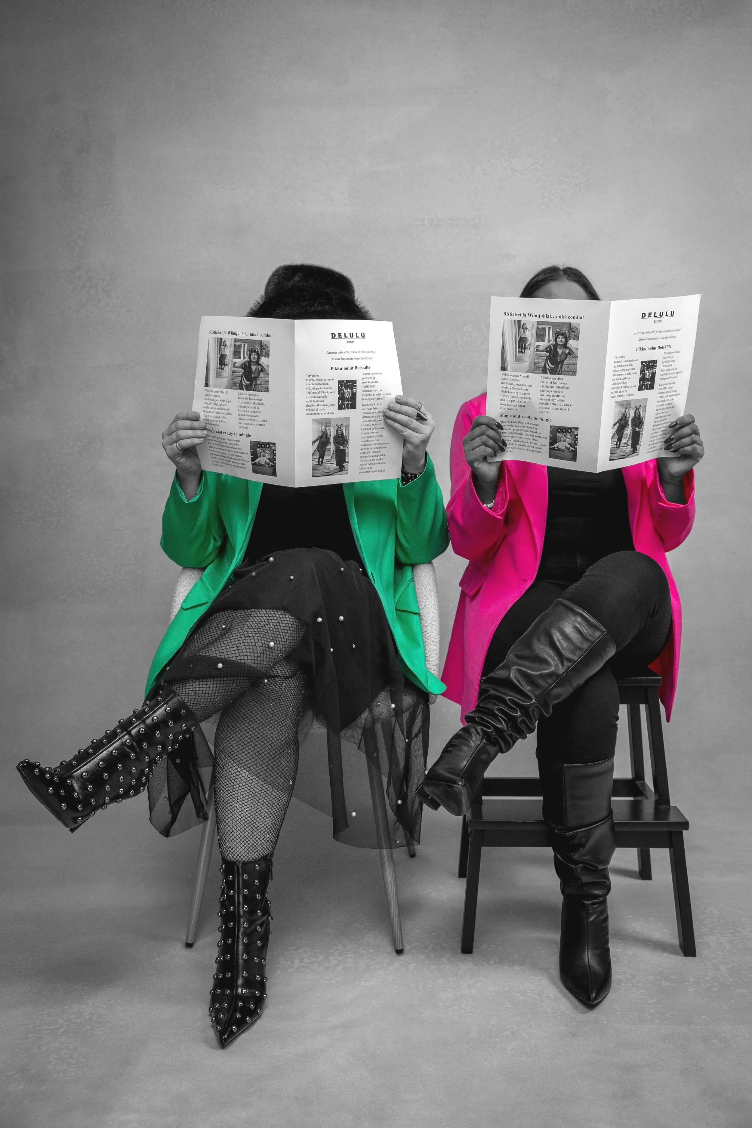 Kuvassa on kaksi naista istumassa tuoleilla piiloutuneina sanomalehtien taakse. He ovat valokuvastudiolla podcastin promokuvauksessa. Valokuva on mustavalkoinen, mutta toisen naisen takki on väriltään vihreä ja toisen naisen takki on väriltään pinkki