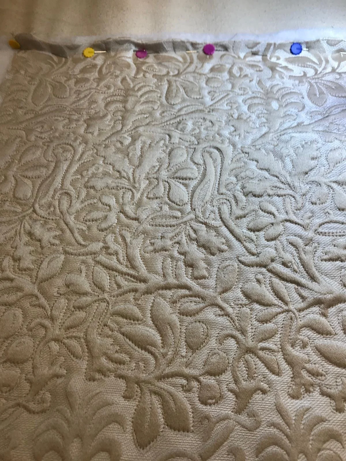 Close-up of an embroidered fabric with a floral and vine pattern, pinned at the top with colorful push pins.