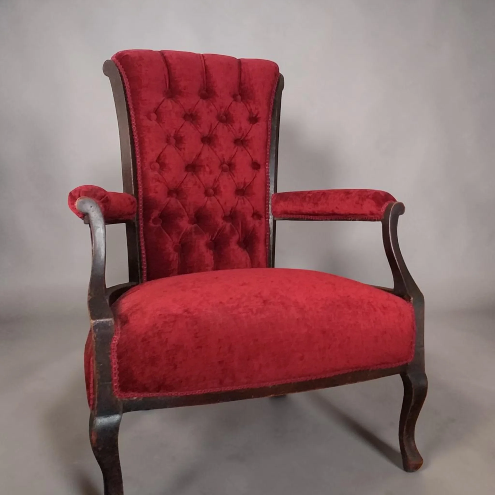 A red velvet upholstered vintage high-back armchair with wooden legs and armrest.