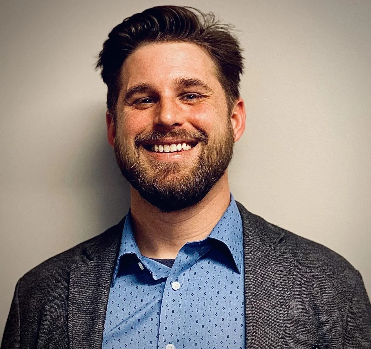 A Caucasian man with light brown hair is smiling with a medium blue collared shirt under a