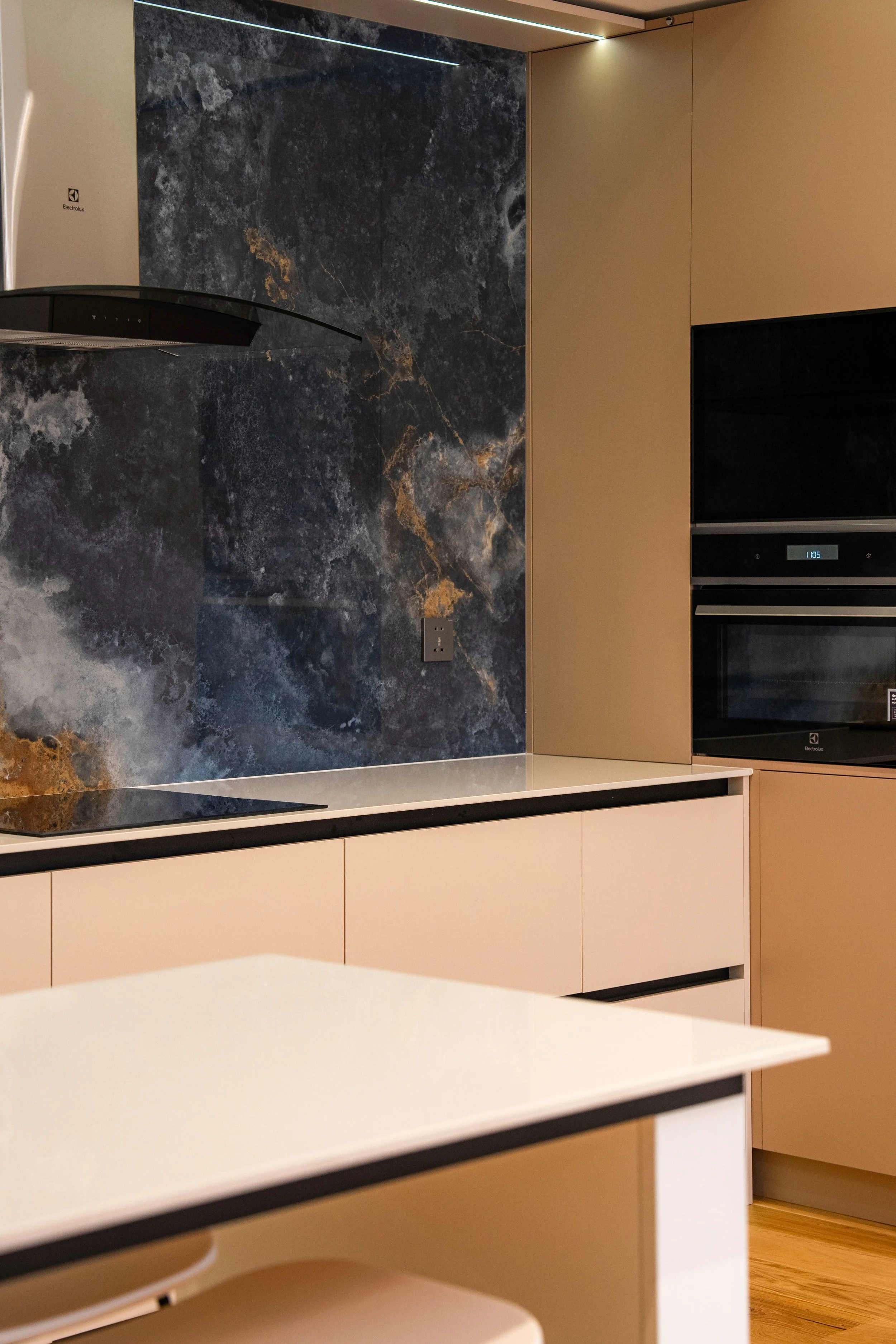 Modern kitchen with beige cabinets, a black marble countertop with gold veining, an Electrolux built-in oven, and a small portion of a white kitchen island with rounded edges and black trim.