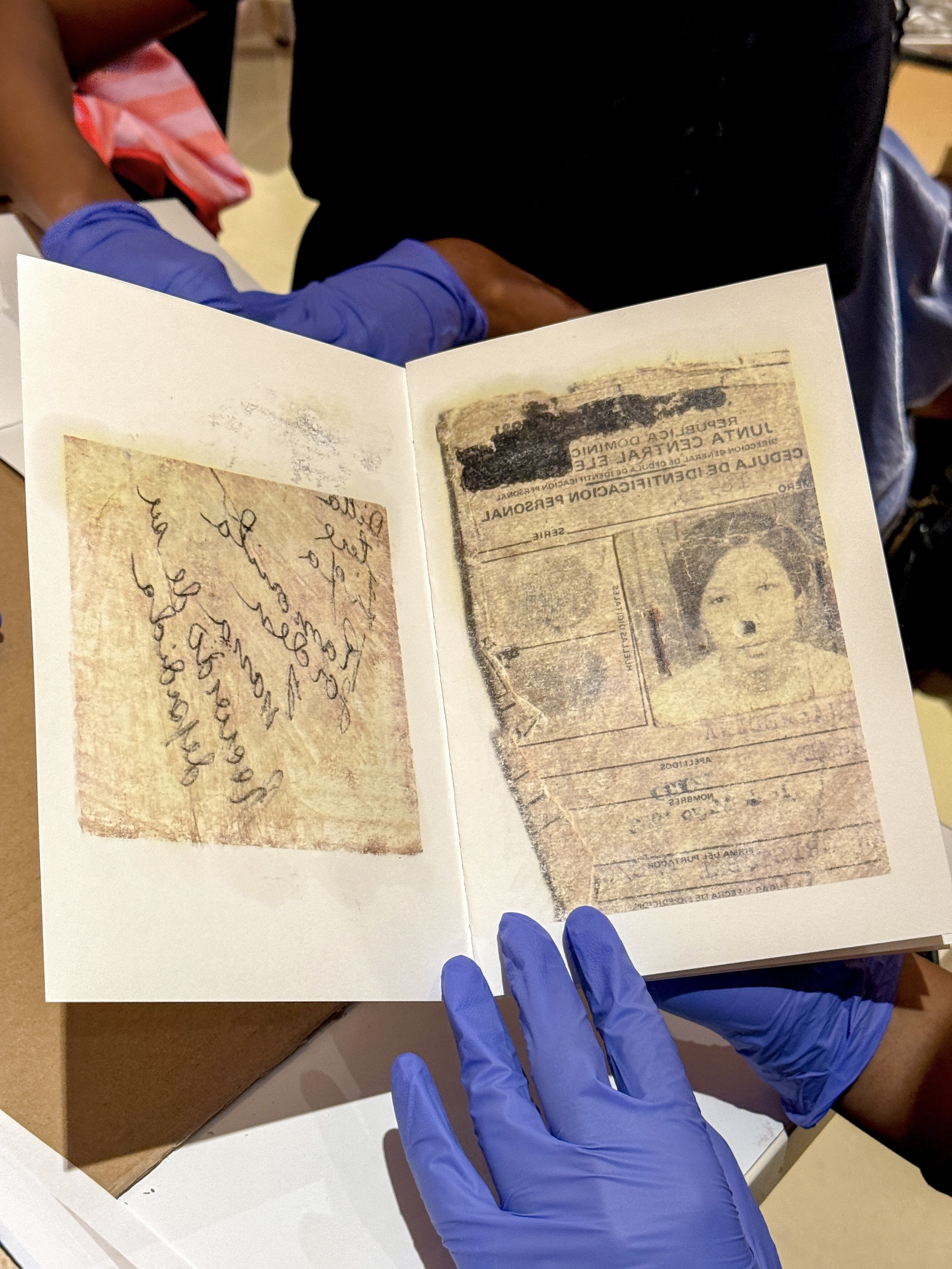 Open passport with old, faded stamps and a photo of a woman, held by a person wearing blue gloves.