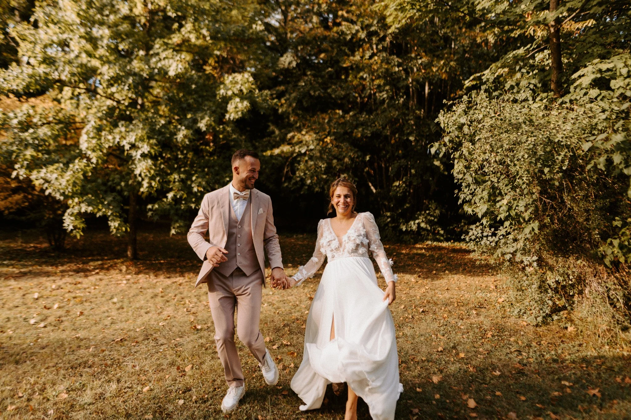 Un couple en tenue de mariage se tenant par la main dans un parc verdoyant, souriant heureux.