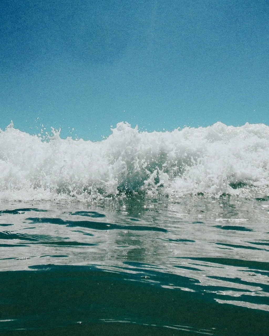 Ocean wave crashing under clear blue sky