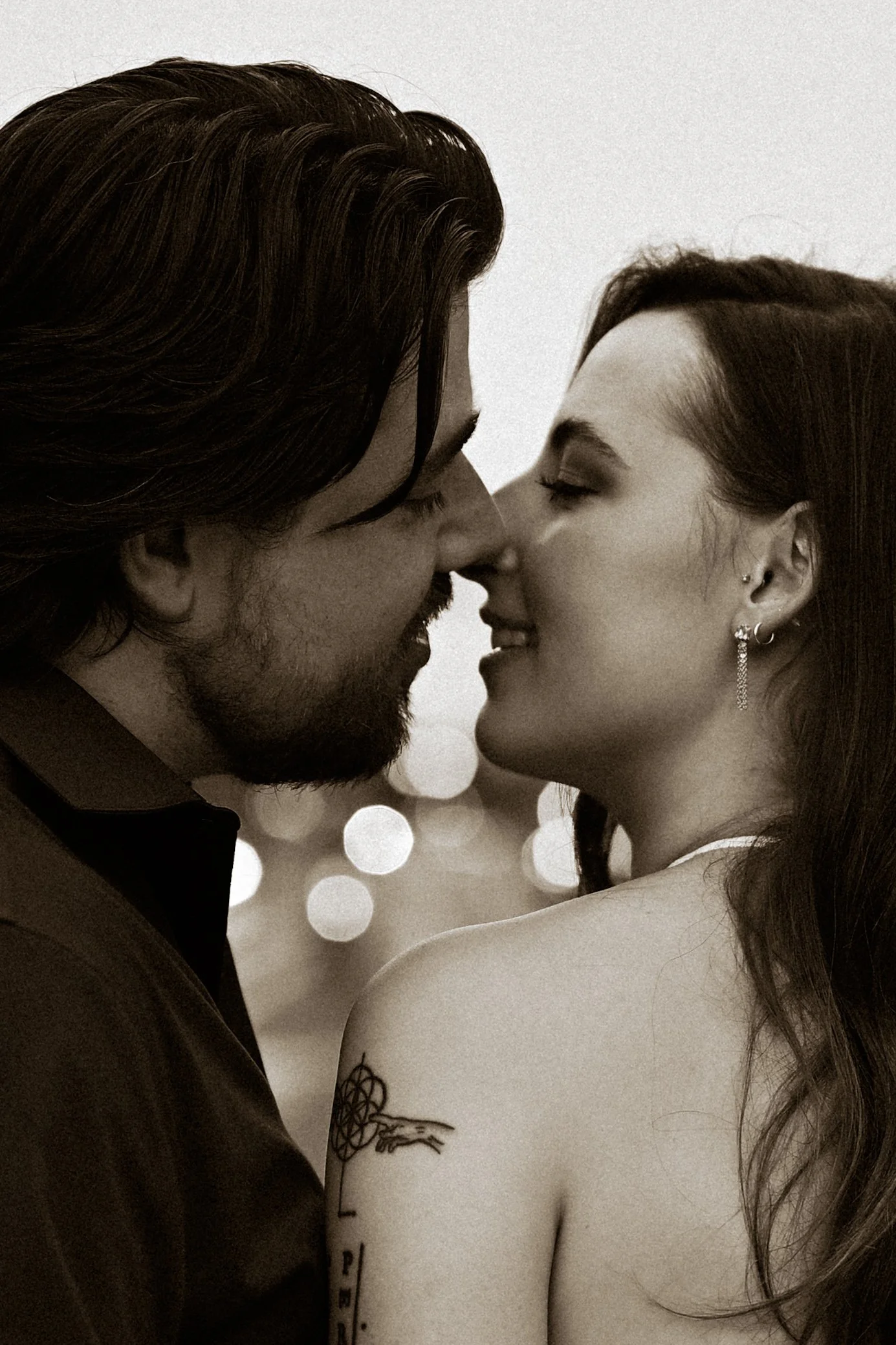A bride and groom kissing outdoors under a wooden arch, with the groom in a black suit and red bow tie and the bride in a white dress.