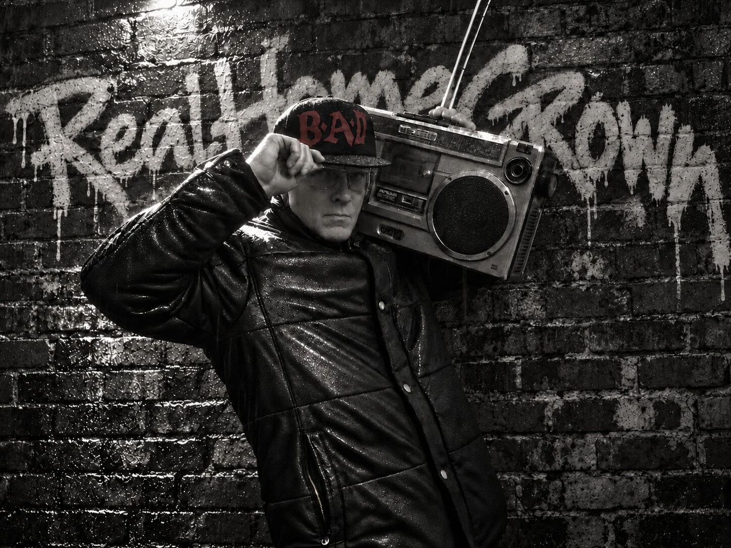 Gary McPherson carrying a boombox in the rain against RealHomeGrown graffiti