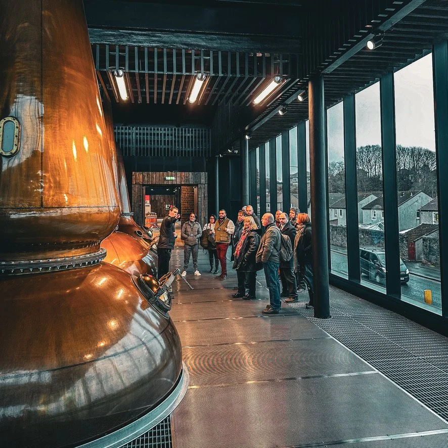 Guests enjoying a guided Scottish whisky distillery tour, learning about traditional whisky production beside large copper pot stills.