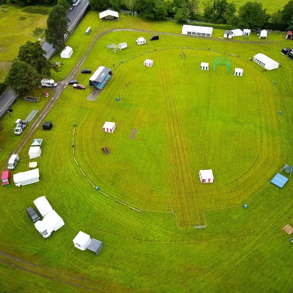 Aerial view of the Luss Highland Gathering field with tents and event setup in progress, surrounded by lush green countryside near Loch Lomond