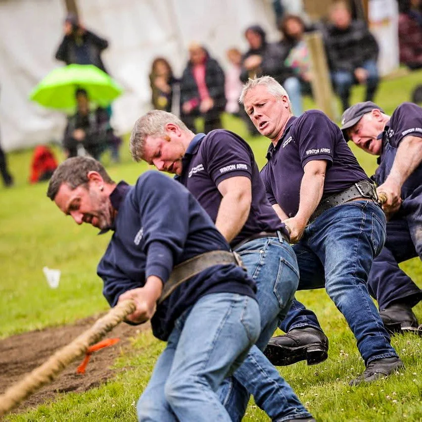 Men competing in a tug of war event at the Luss Highland Gathering, a traditional strength contest held on the grassy games field