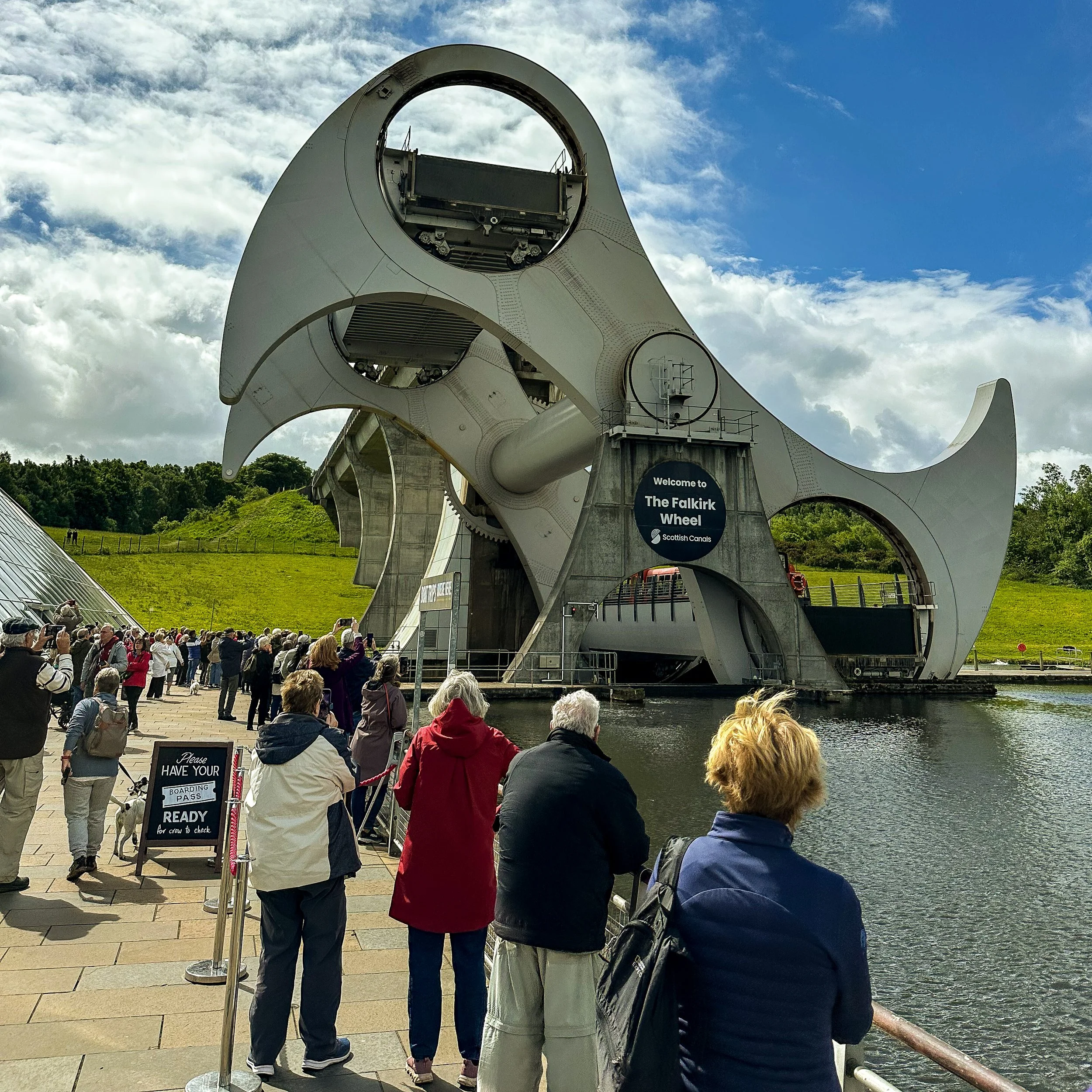 Visitors admiring the Falkirk Wheel, Scotland's remarkable rotating boat lift, beside the canal on a bright day.