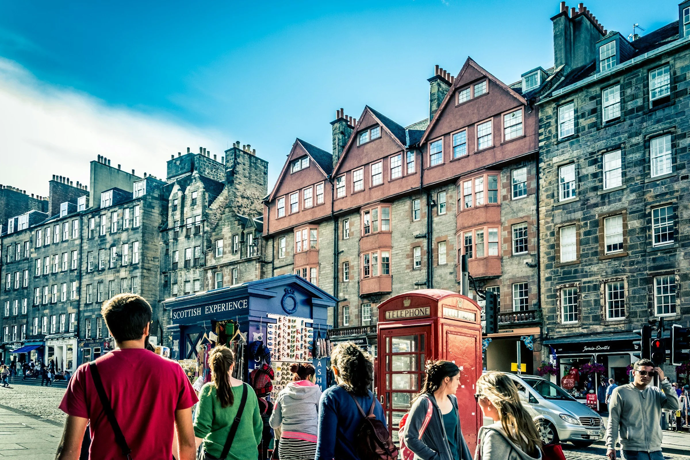Visitors exploring Edinburgh's historic Royal Mile, with traditional Scottish stone buildings, shops and a red telephone box in the Old Town.