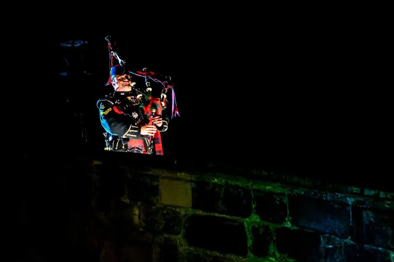 Lone piper illuminated against the night sky, performing atop the ramparts of Edinburgh Castle to close the Royal Edinburgh Military Tattoo.