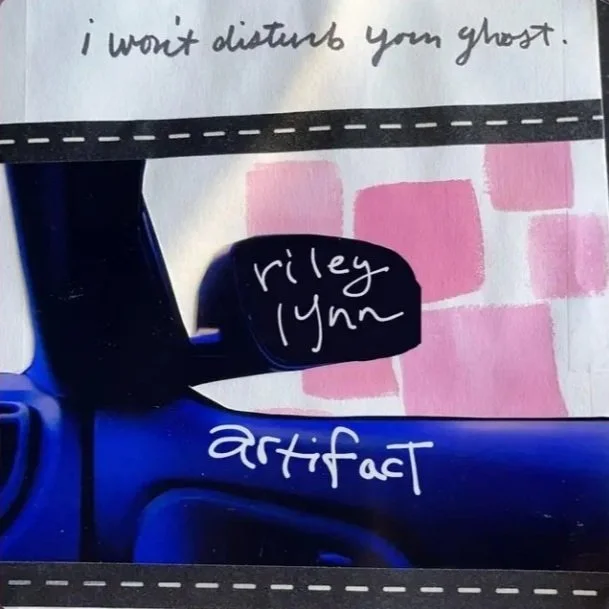 Close-up of a blue object with handwritten notes on it, including the phrases 'i won't disturb your ghost', 'riley lynn', and 'artifact', with a background of pink squares.