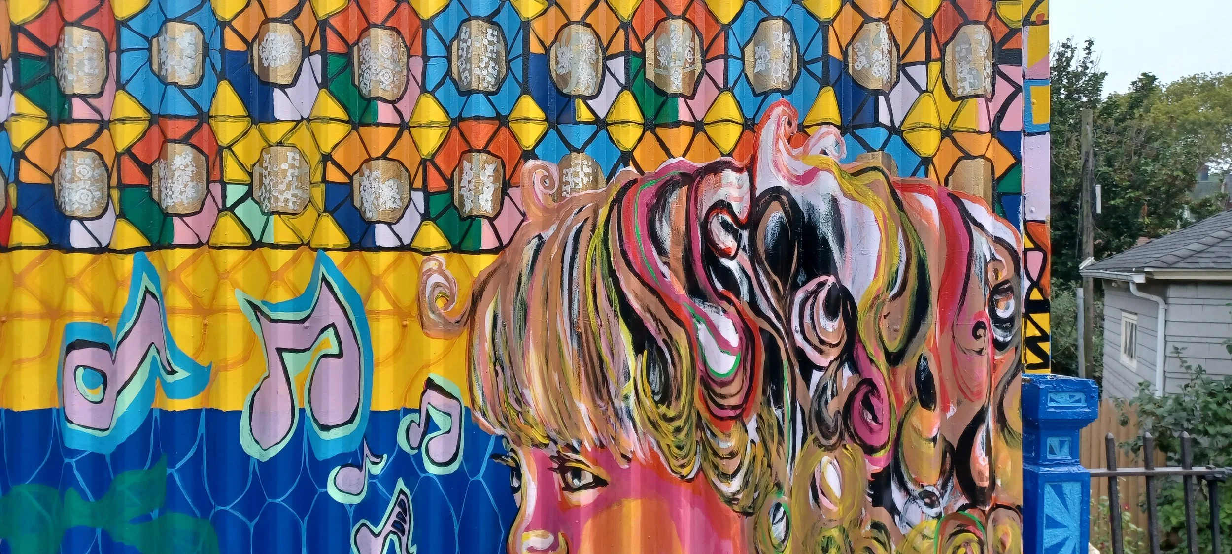 Colorful mural featuring a woman's face with curly hair, musical notes, and a vibrant geometric background.