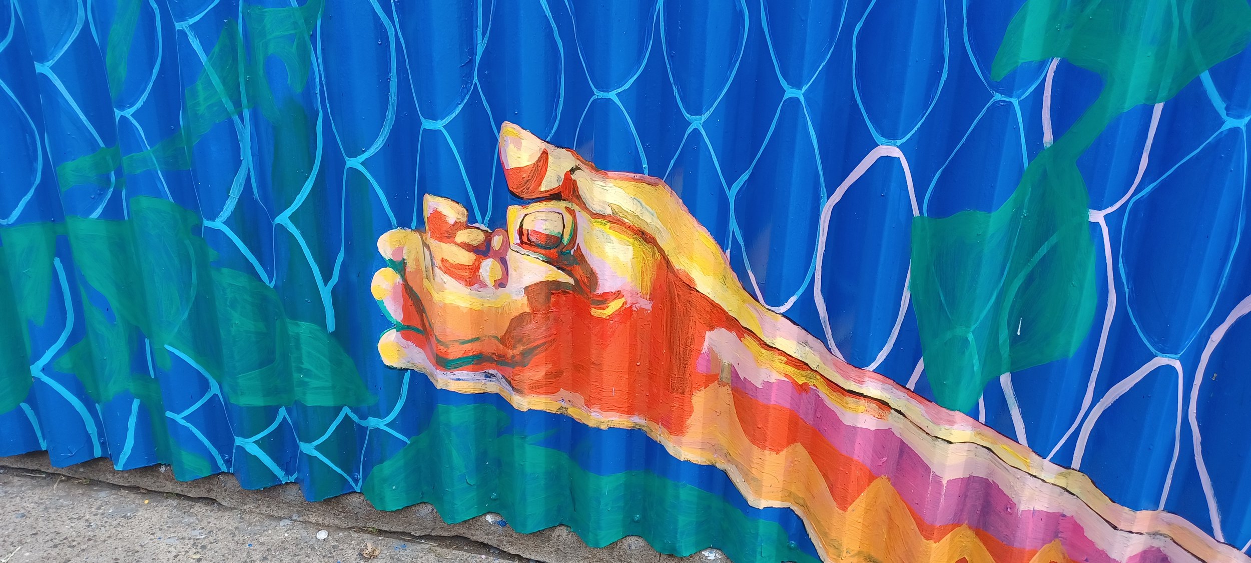 Colorful mural painting of a hand holding a paintbrush against a blue background with green accents.