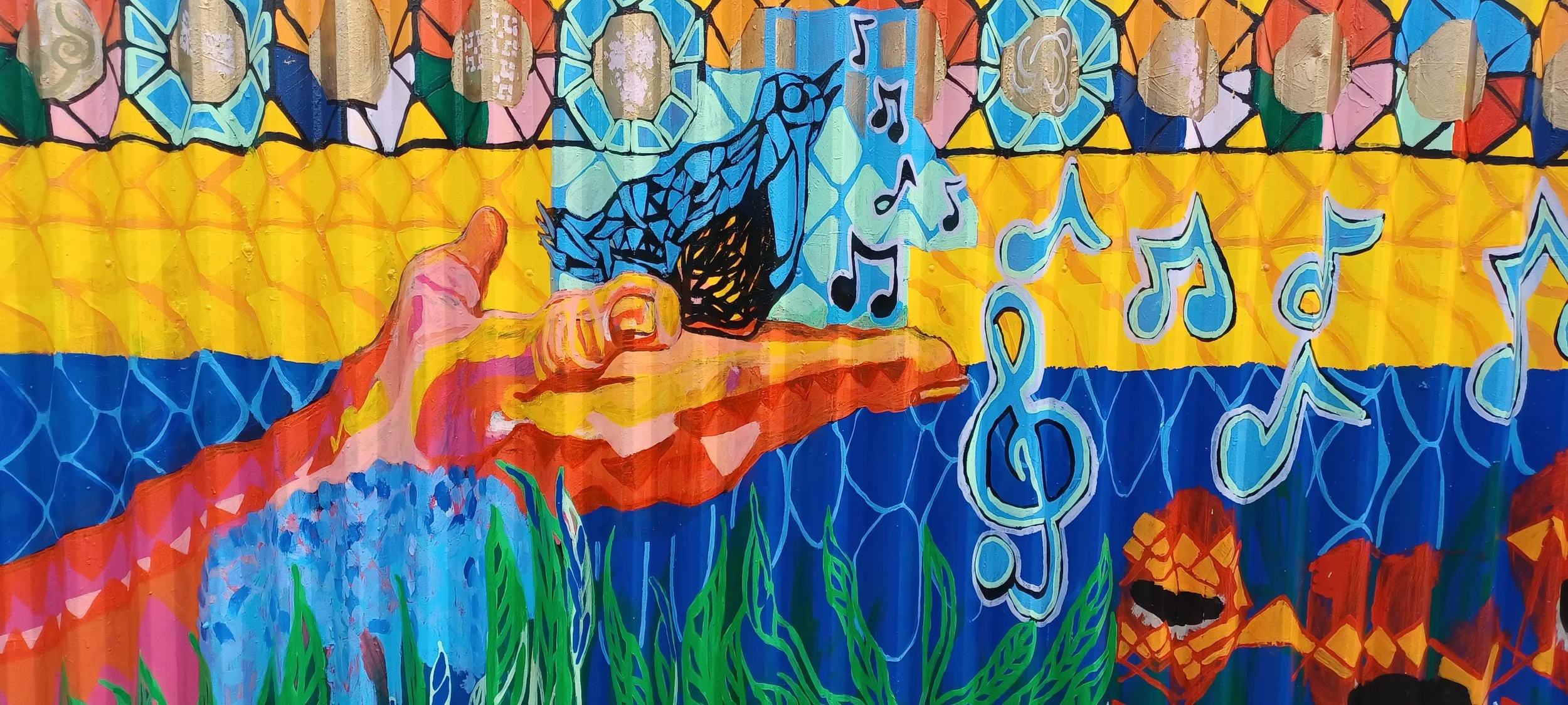 Colorful mural featuring a hand pointing towards a computer with musical notes and a dog silhouette on the screen, decorative patterns, and abstract elements in bright colors.