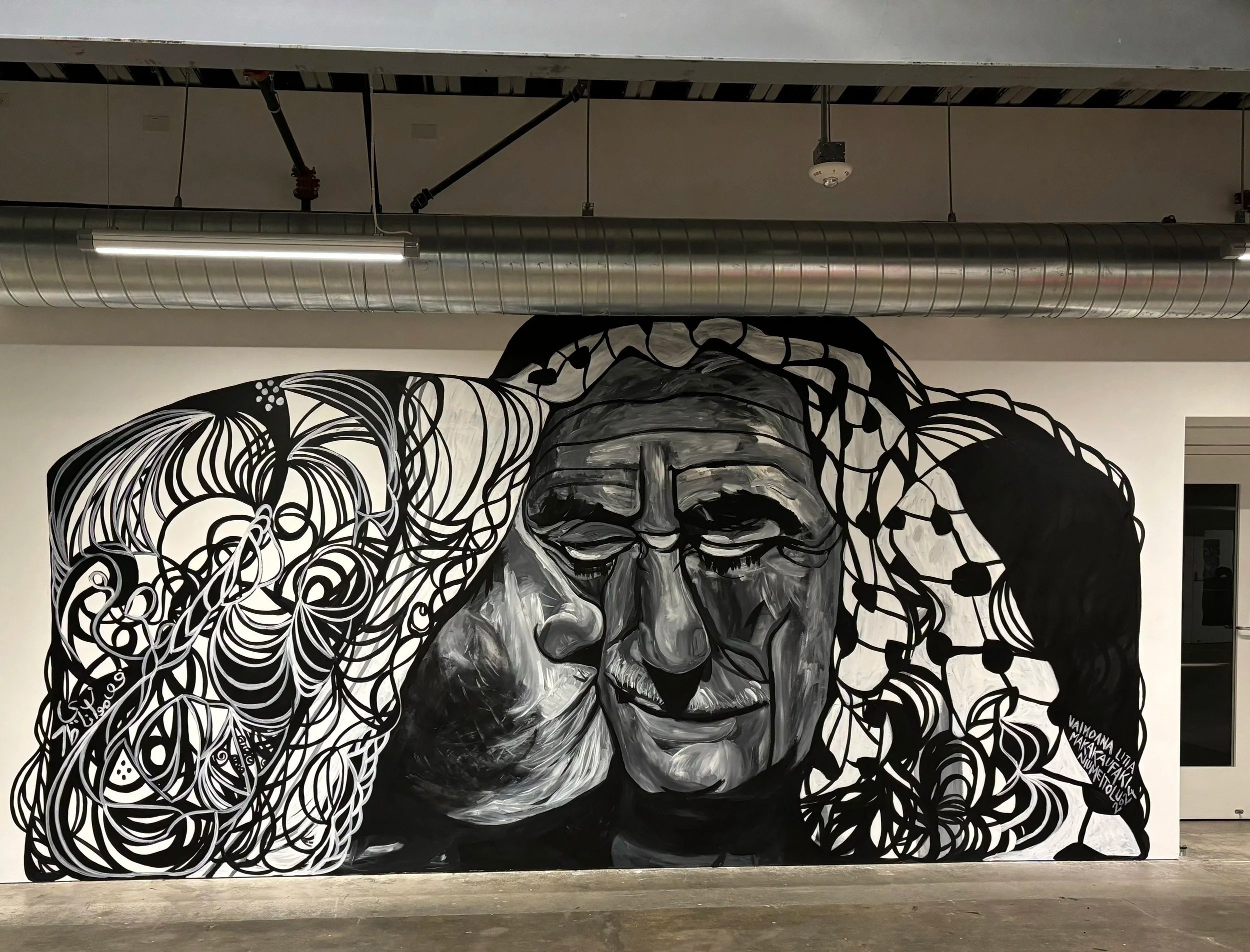 Black and white mural of a woman with long, flowing hair, with the left side composed of intricate, swirling patterns, and the right side showing detailed facial features with closed eyes.