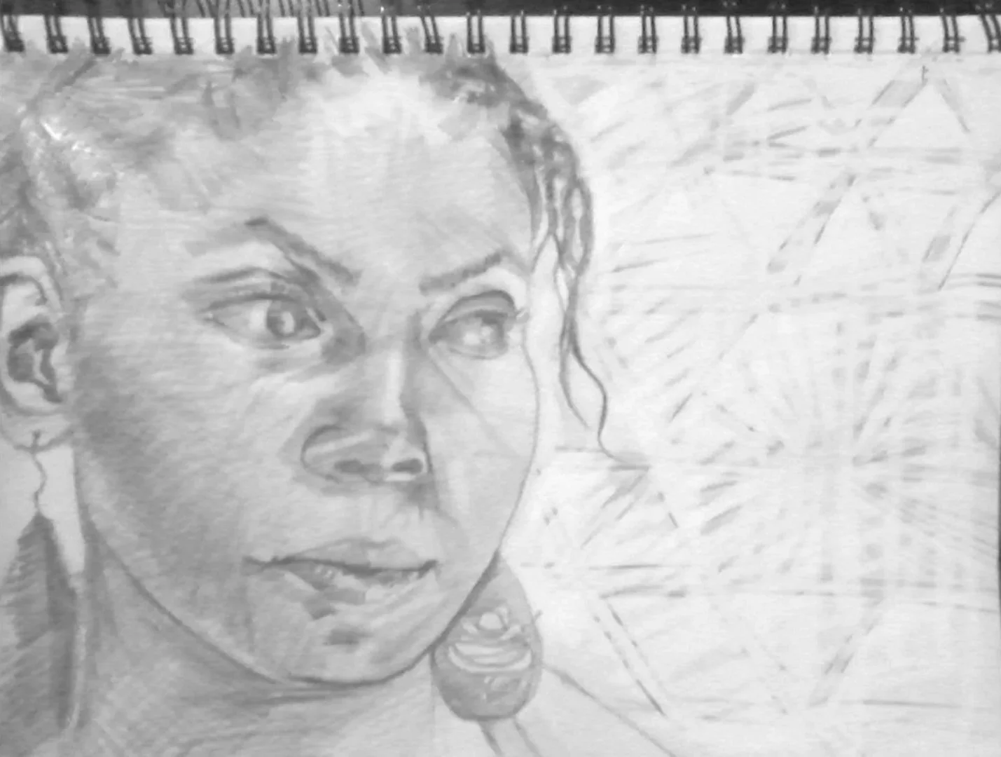A pencil sketch of a woman's face, with detailed eyes, eyebrows, nose, and lips, and some earrings visible, on a spiral-bound notebook paper.