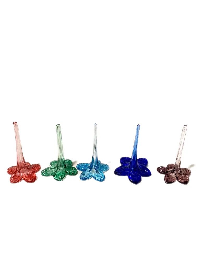 Five colorful glass flower-shaped stirring sticks arranged in a row, in pink, green, blue, dark blue, and clear colors on a white background.
