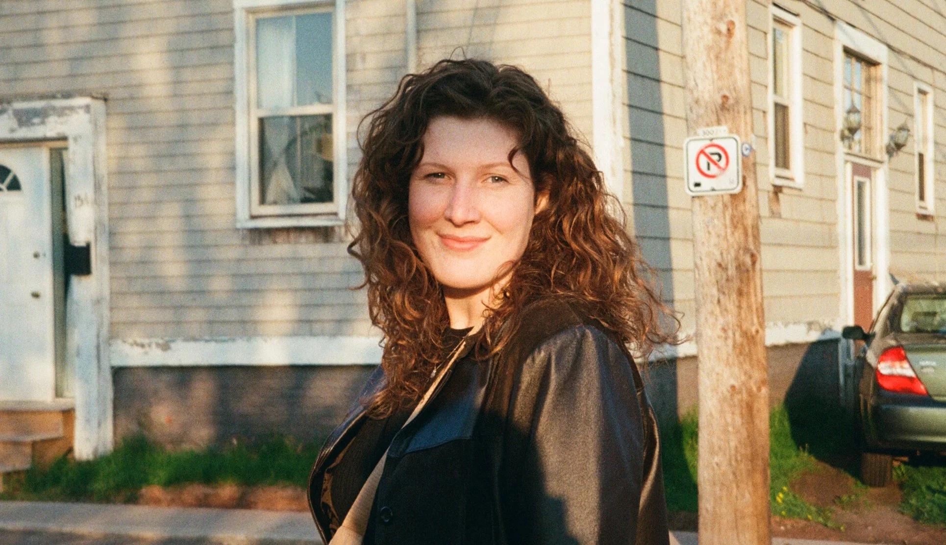 Samantha has long brown curly hair and is waring a leather jacket