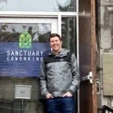 Rob is standing outside Sanctuary Coworking office with logo on glass door.