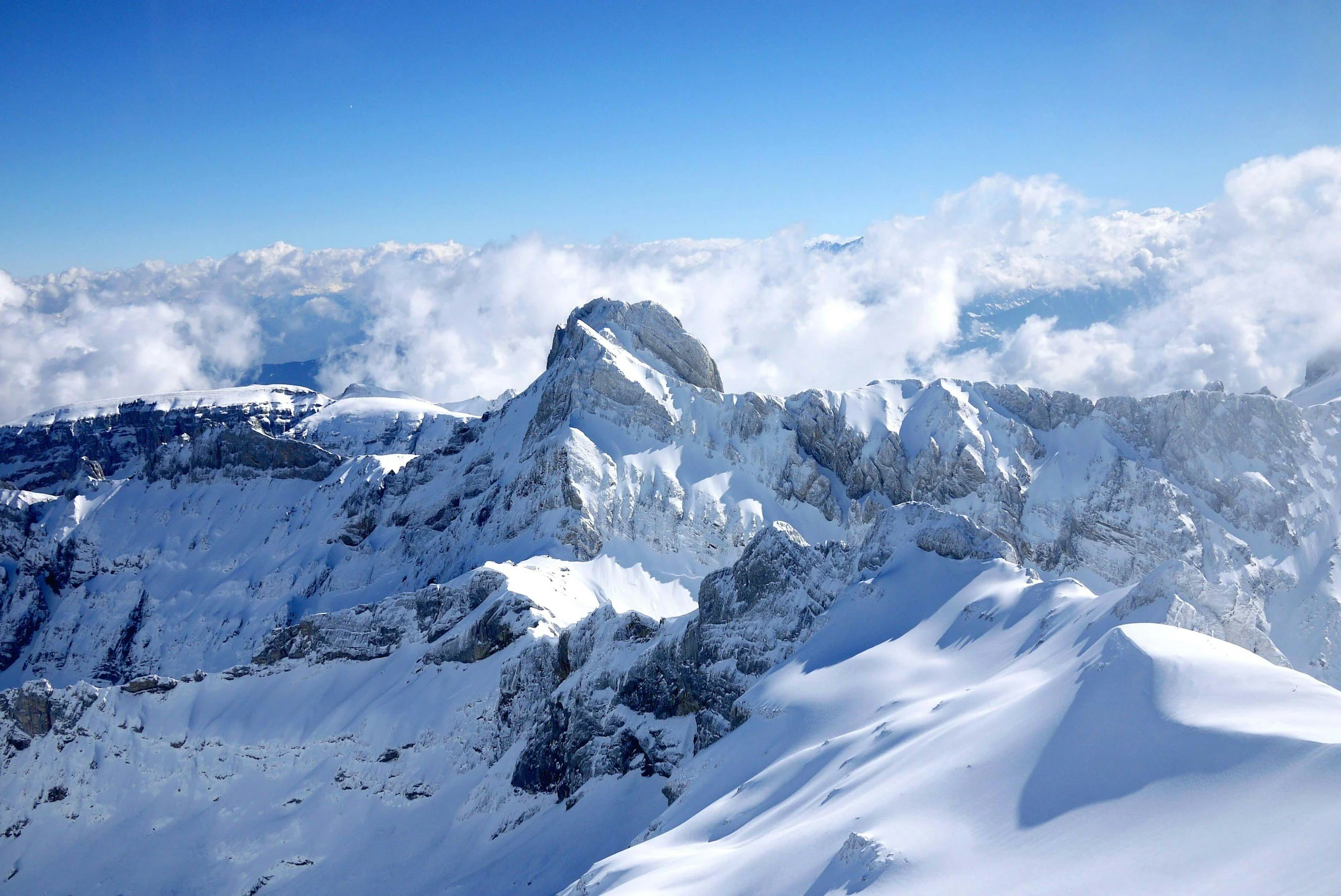 Snow-covered mountain peaks with a blue sky and clouds in the background.