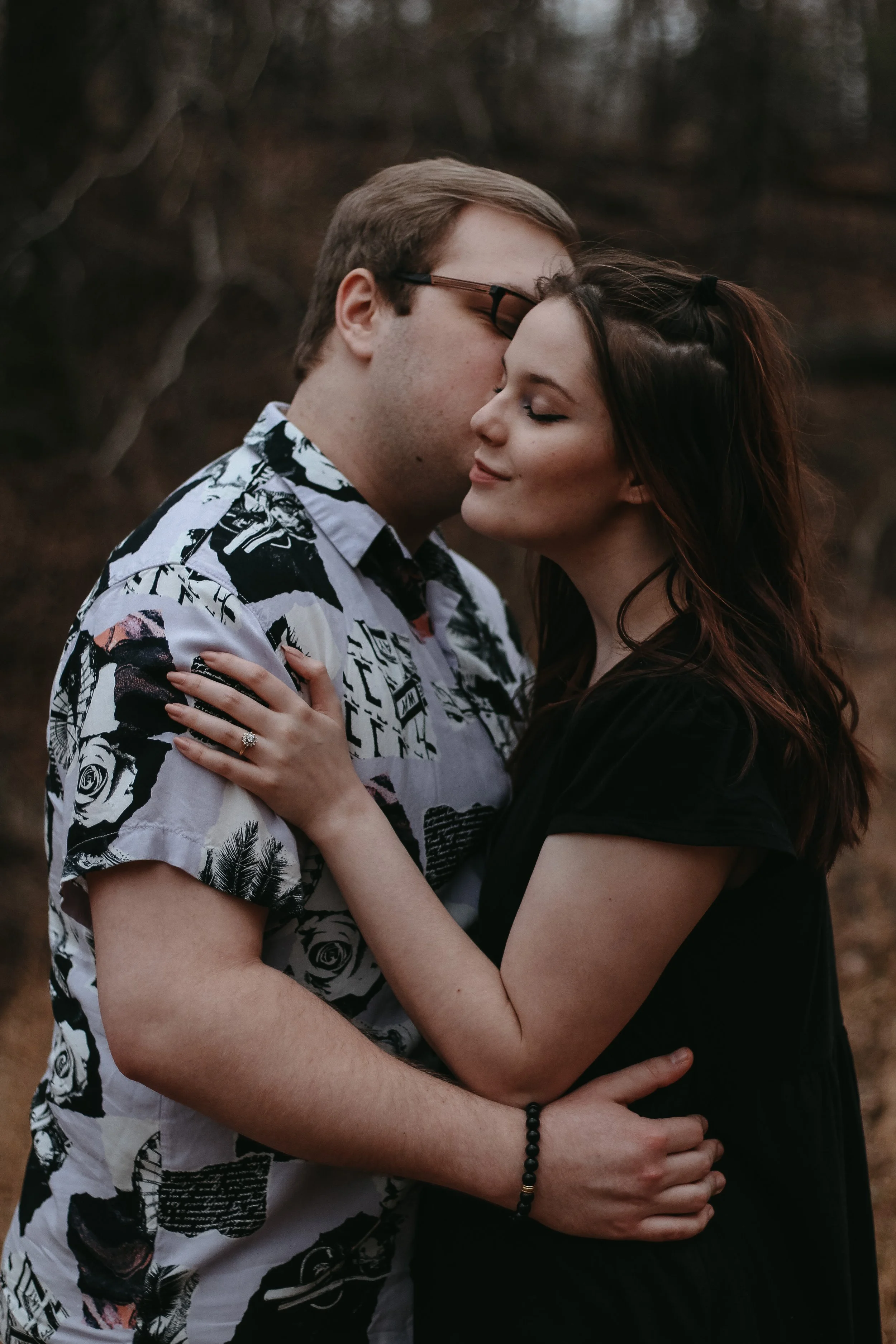 A young couple embraces outdoors, with their foreheads touching and eyes closed, in a tender moment.