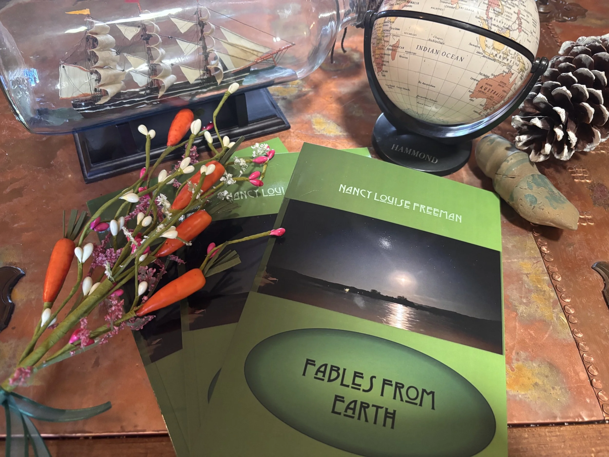 Book titled "Fables From Earth", surrounded by world globe, ship in a bottle, assorted sundries.
