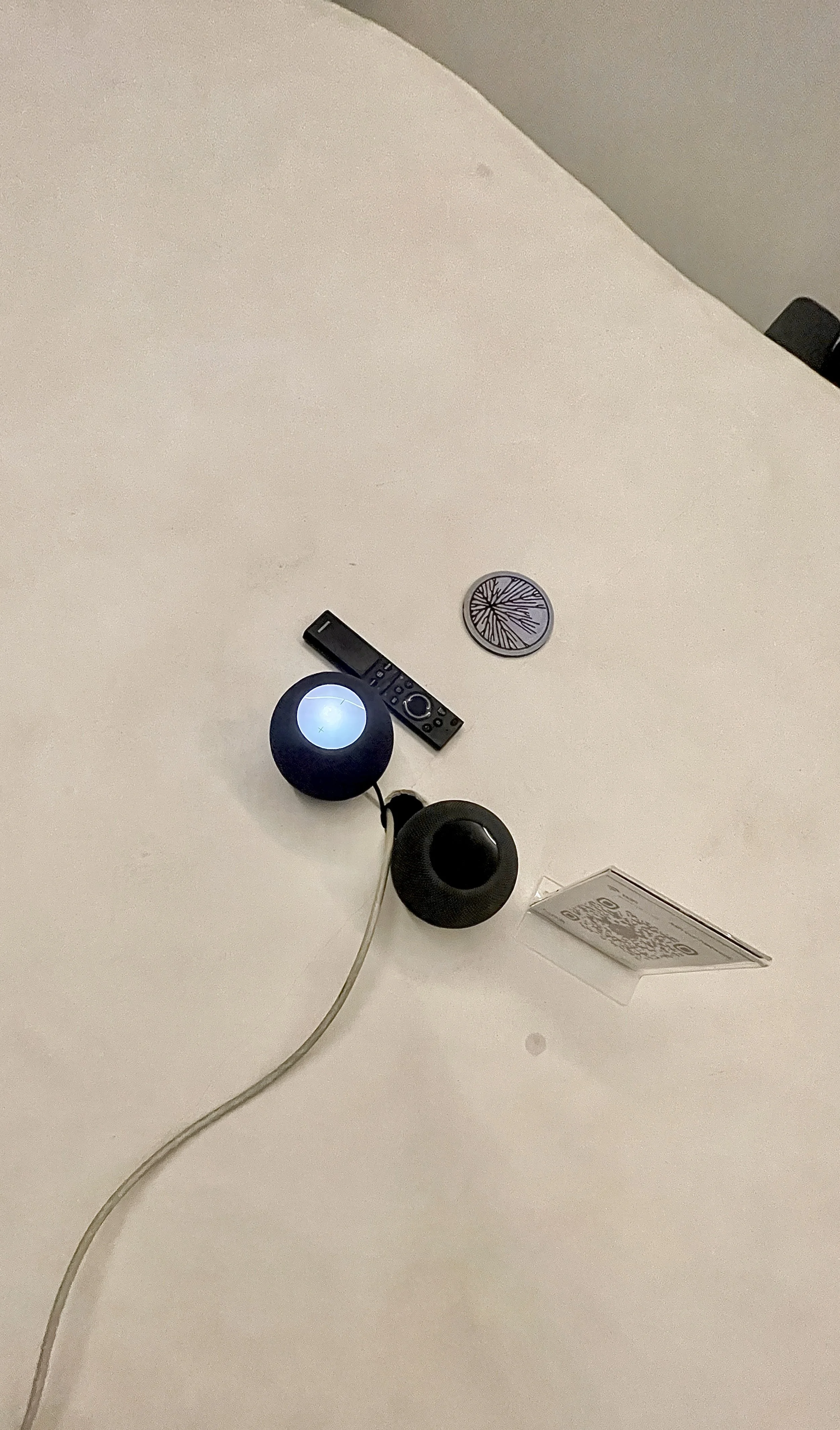 Objects on a white table including a remote control, a black speaker, a spherical device, a QR code sign, and a round decorative item. Hypha Inc Marketing Agency and Creative Studio Lab, Tulum.