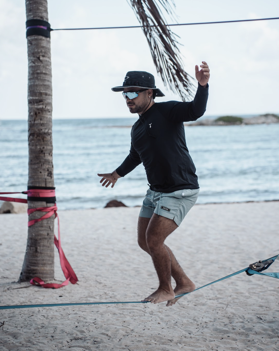 A man balancing on a slackline tied to a palm tree on a beach.
