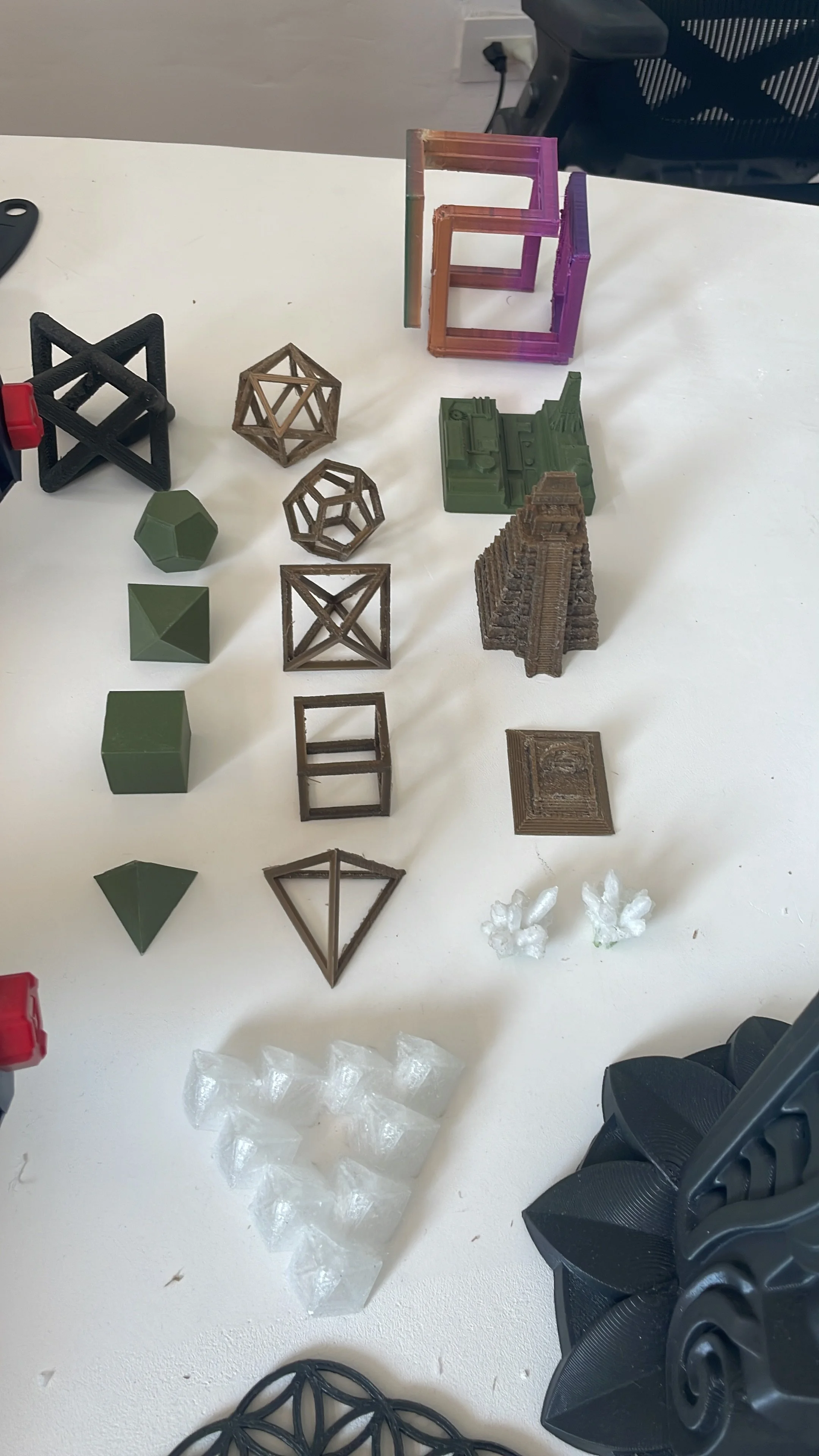 Collection of small 3D-printed models of geometric shapes, structures, and objects arranged on a white table. Hypha Inc Marketing Agency and Creative Studio Lab, Tulum.