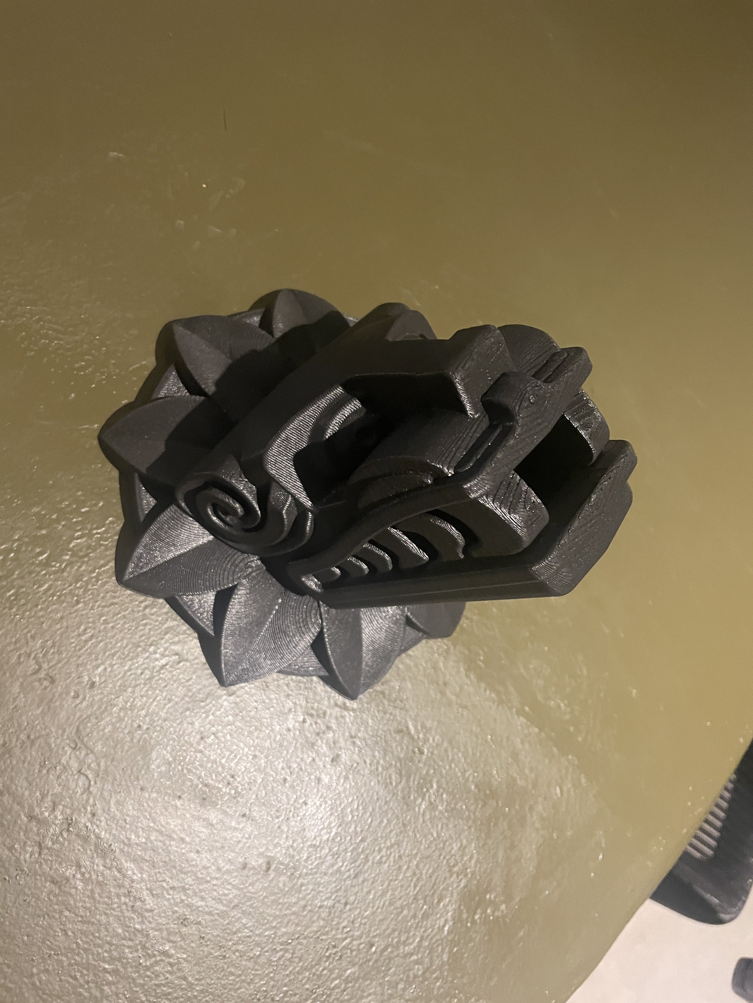 A 3D-printed black origami rose with an intricate design, placed on a textured green surface. Hypha Inc Marketing Agency and Creative Studio Lab, Tulum.