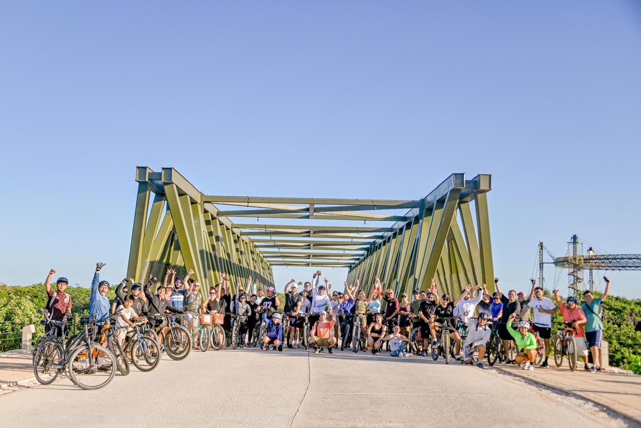 Group of people with bicycles under a green bridge on a sunny day