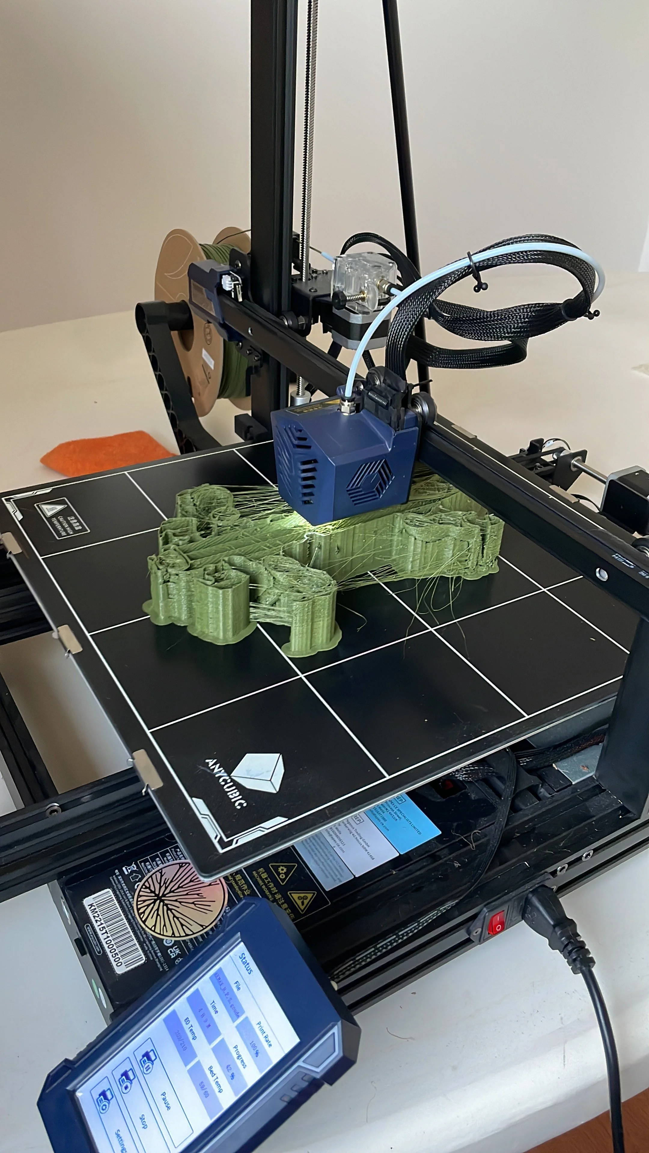 A 3D printer printing a green object with intricate details on the print bed, connected to a control panel displaying status and parameters. Hypha Inc Marketing Agency and Creative Studio Lab, Tulum.