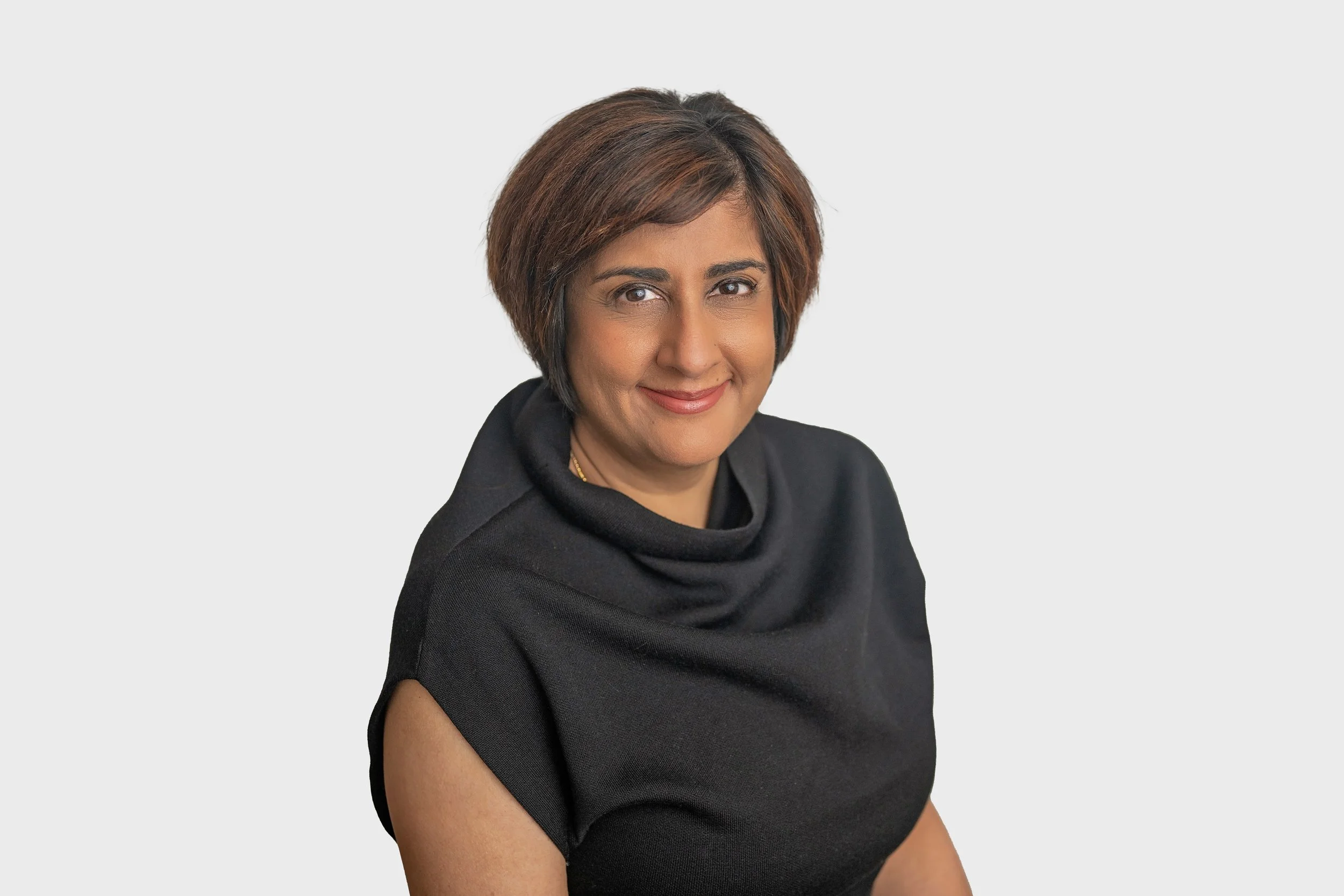 A woman with short brown hair wearing a black top with a cowl neck, smiling against a plain light background.