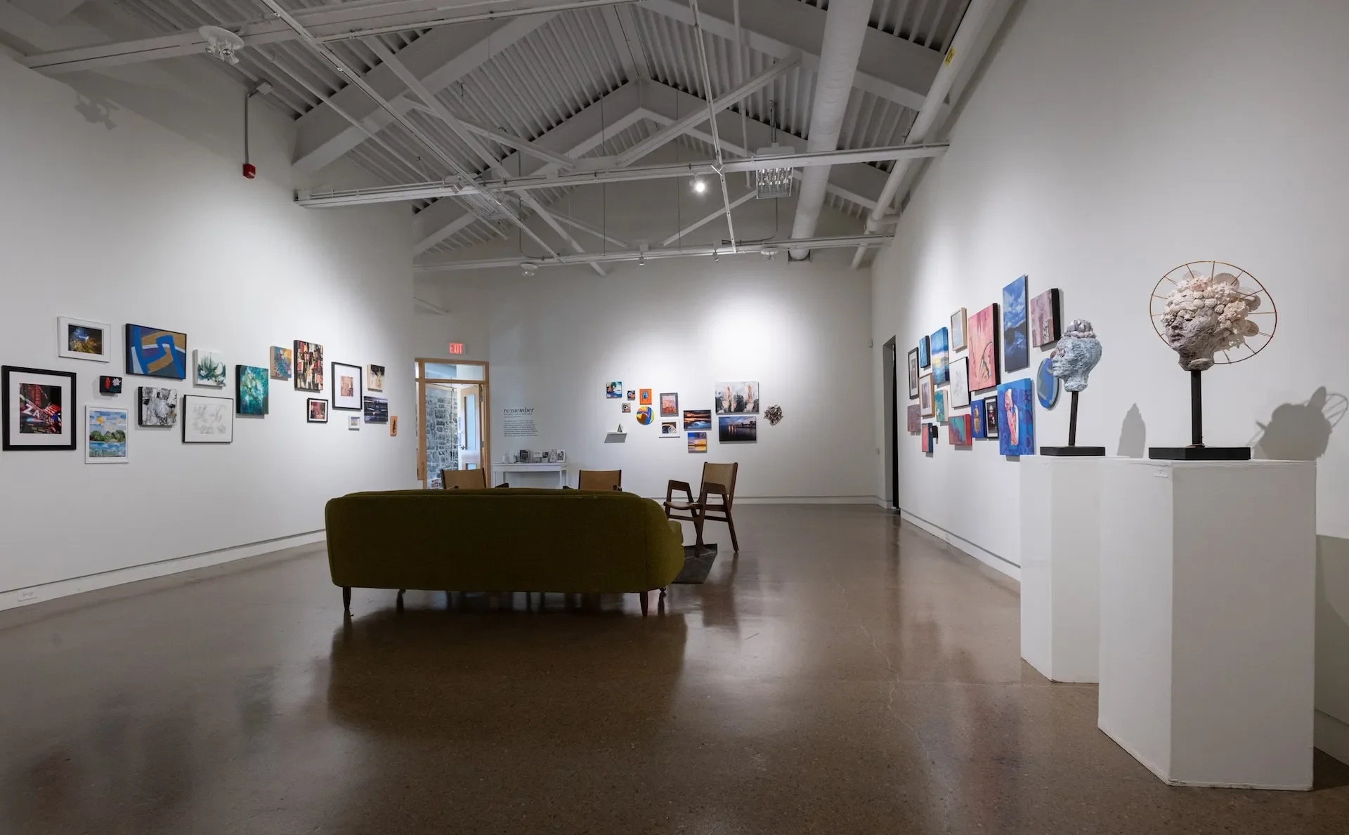 An art gallery with white walls decorated with various paintings and sculptures, and a seating area with chairs and a couch.