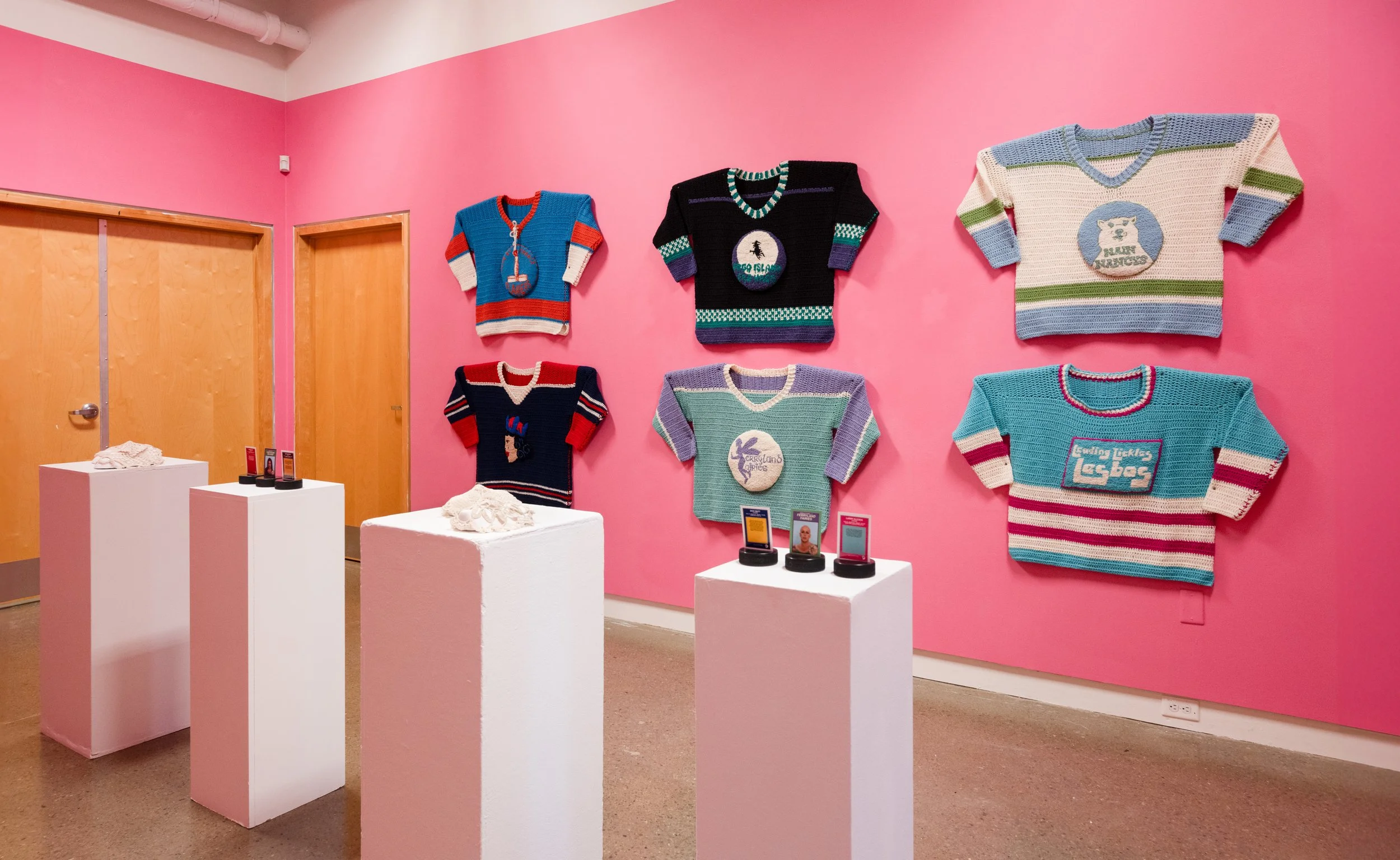 4 plinths with mixed media pieces placed on them. Alongside 6 knitted hockey jerseys hung on the hot pink walls in the State of Flux Gallery.