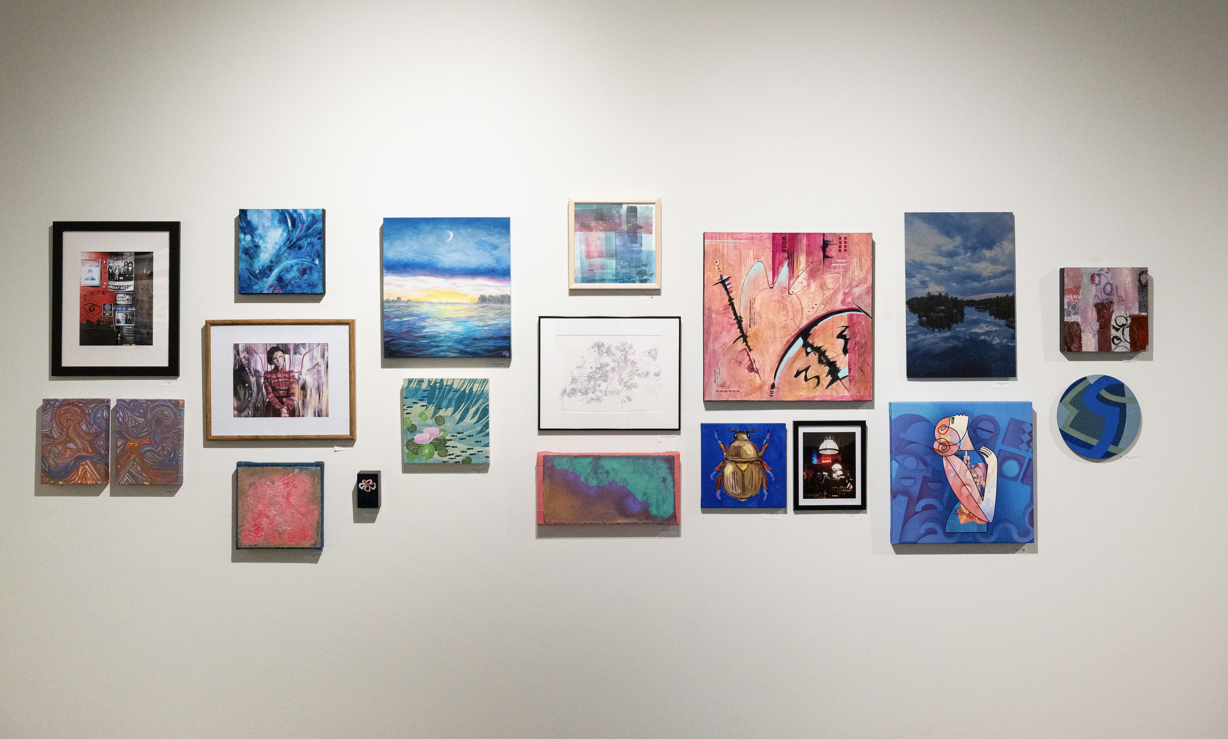 Wall with a diverse collection of framed paintings and artworks, including landscapes, abstract art, and portraits, arranged in a gallery setting.