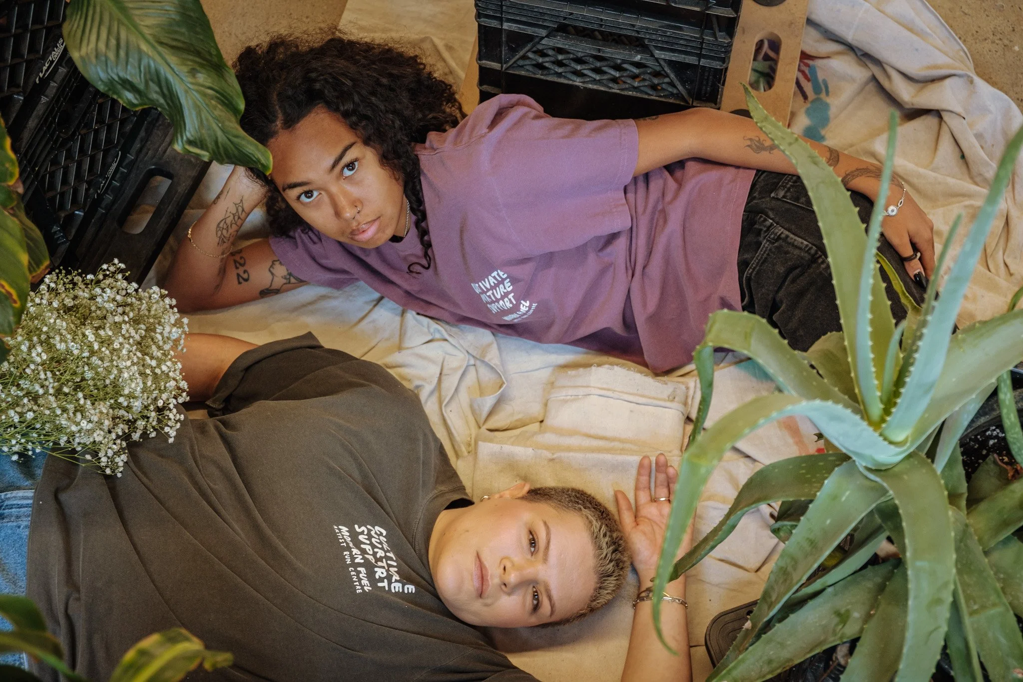 2 woman laying against linen cloth and plants wearing Modern Fuel graphic tees