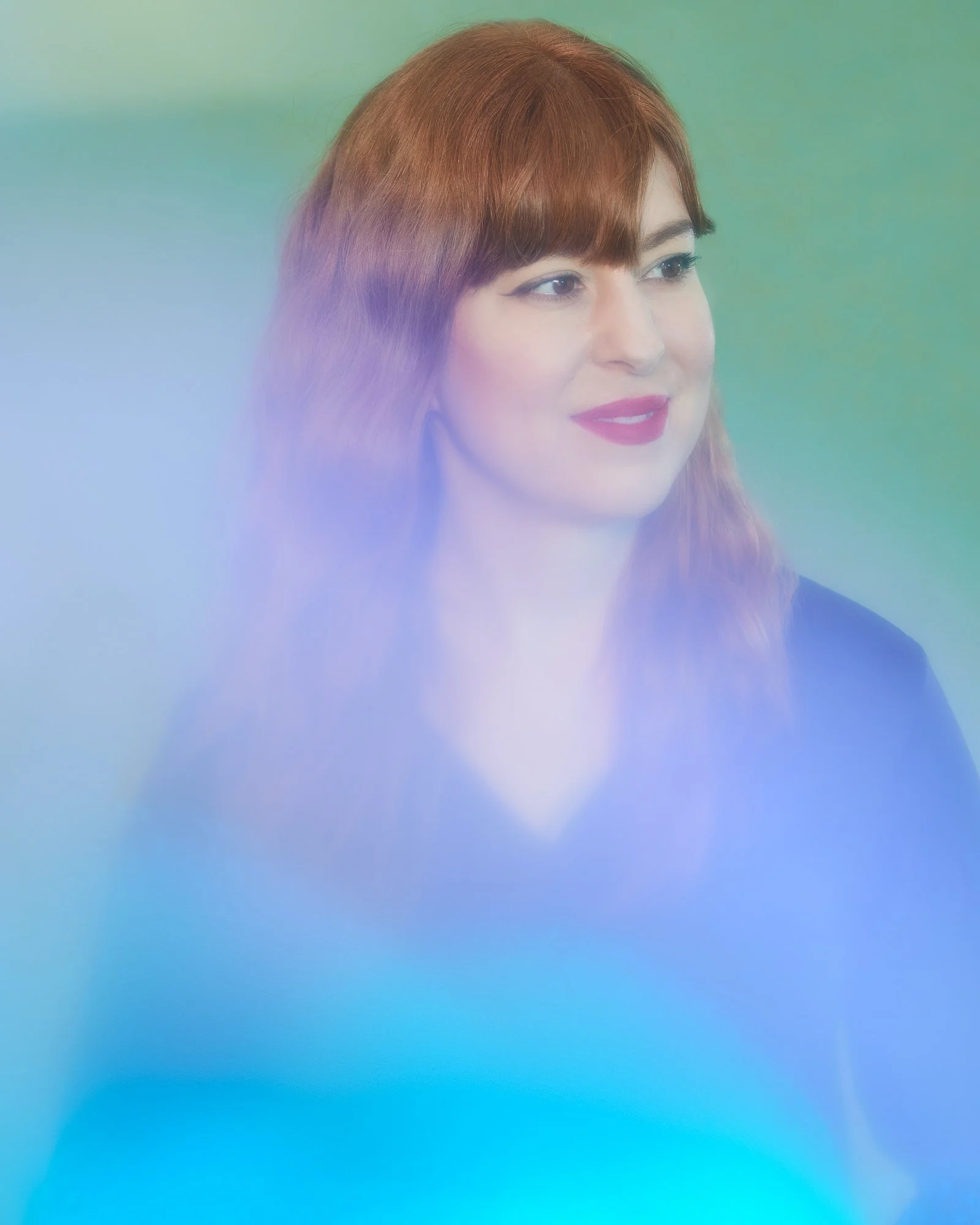 A woman with red hair and makeup looking to the right, with a colored gradient overlay.